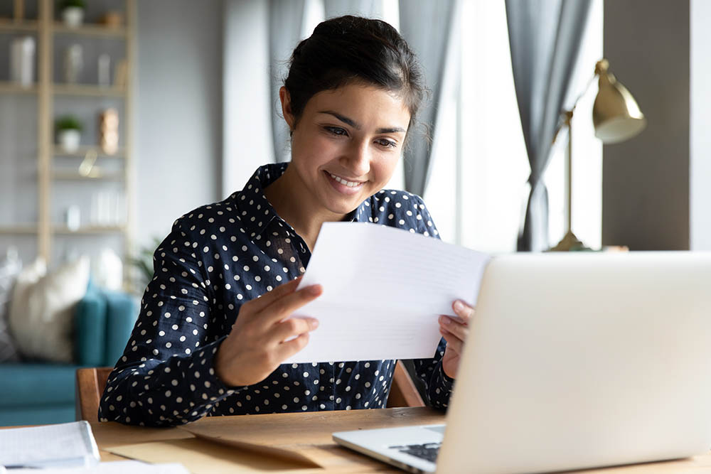 Lower Bills – Action of Energy Cambridgeshire Smiling woman holding energy bill letter sitting at table